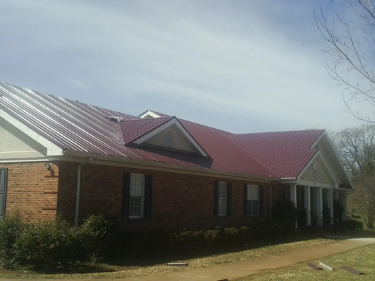 Red metal roof with gabled entries on a long brick building, from a Hail Damage Roof Repair job in Henefer