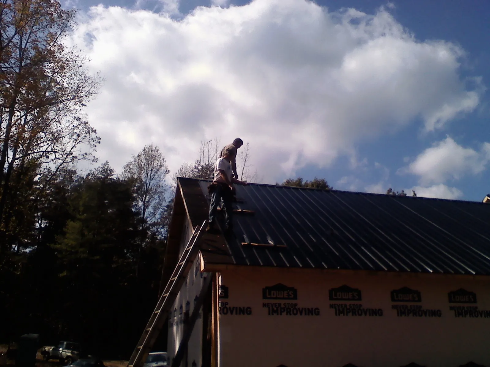 Roofer fastening dark metal panels high against a cloudy sky, from a Roof Inspection job in Henefer