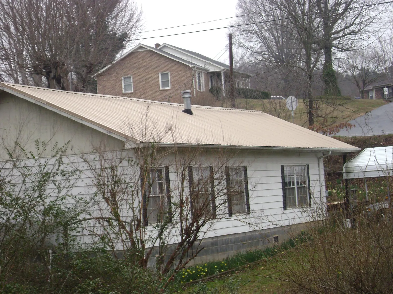 Tan metal roof on a white sided house set into a hillside — Commercial Roofing by Roofing Brothers in Henefer