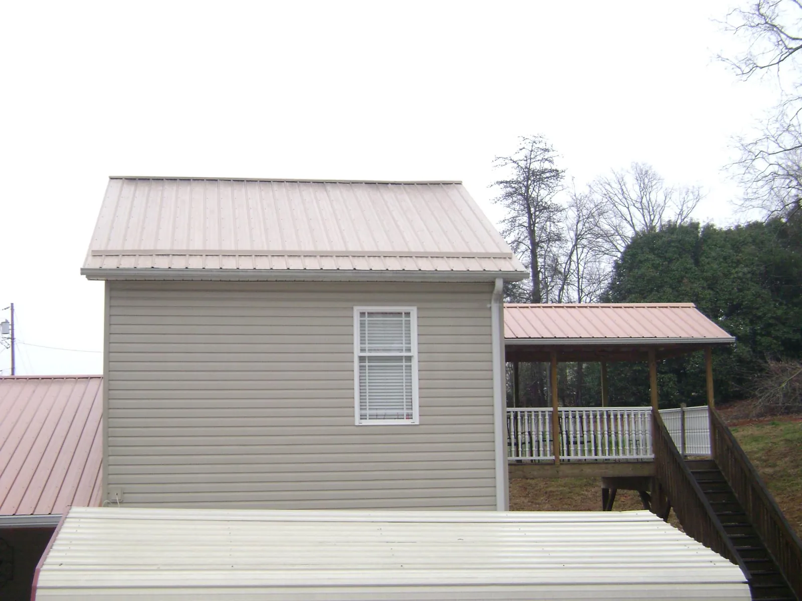 Tan metal roofs on a two story addition and attached porch, from a Roof Replacement job in Henefer